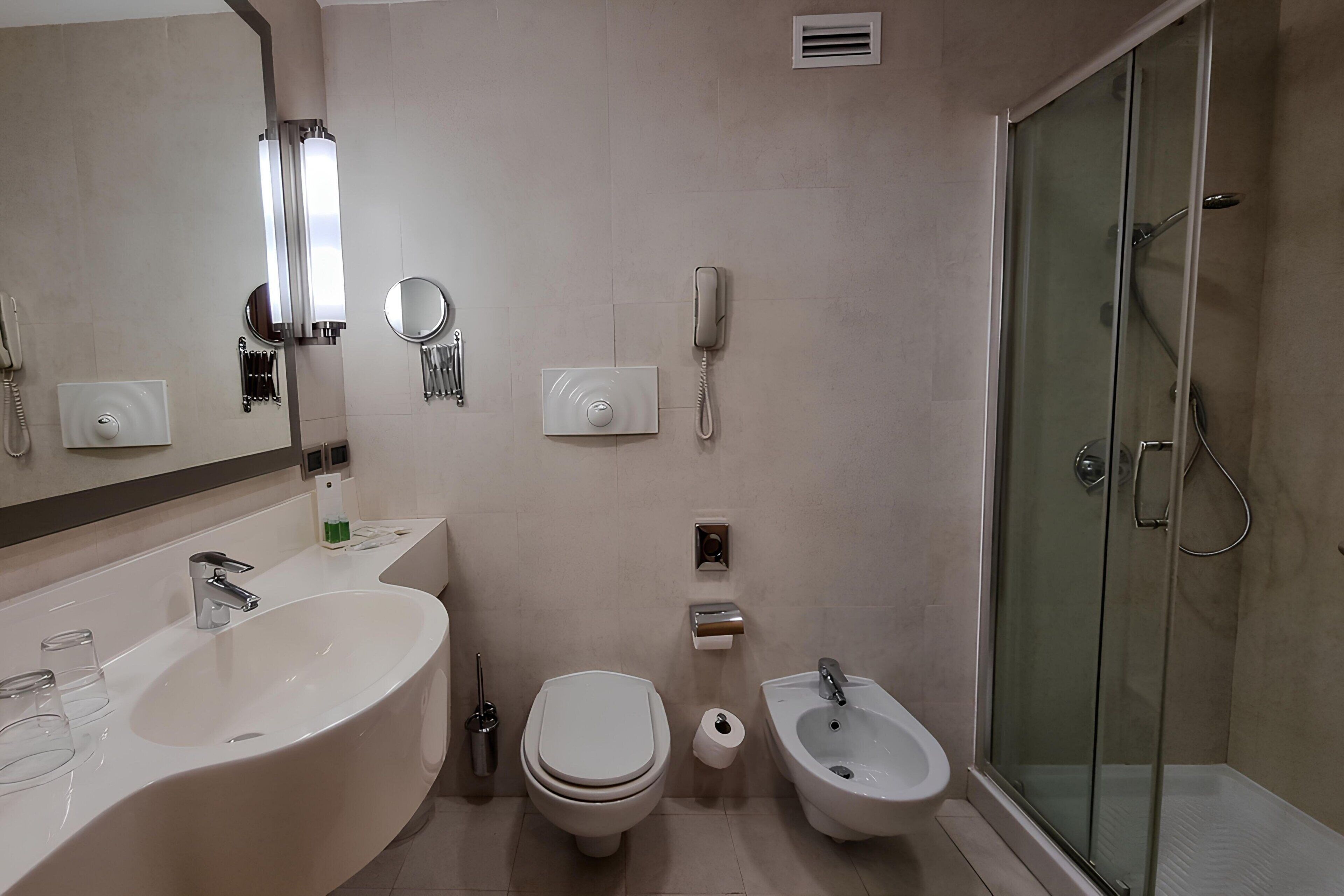 A bathroom with a large sink, toilet, bidet, and a glass-enclosed shower.