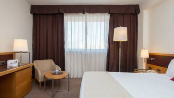 Una habitación de hotel con cama, escritorio, silla y dos lámparas.