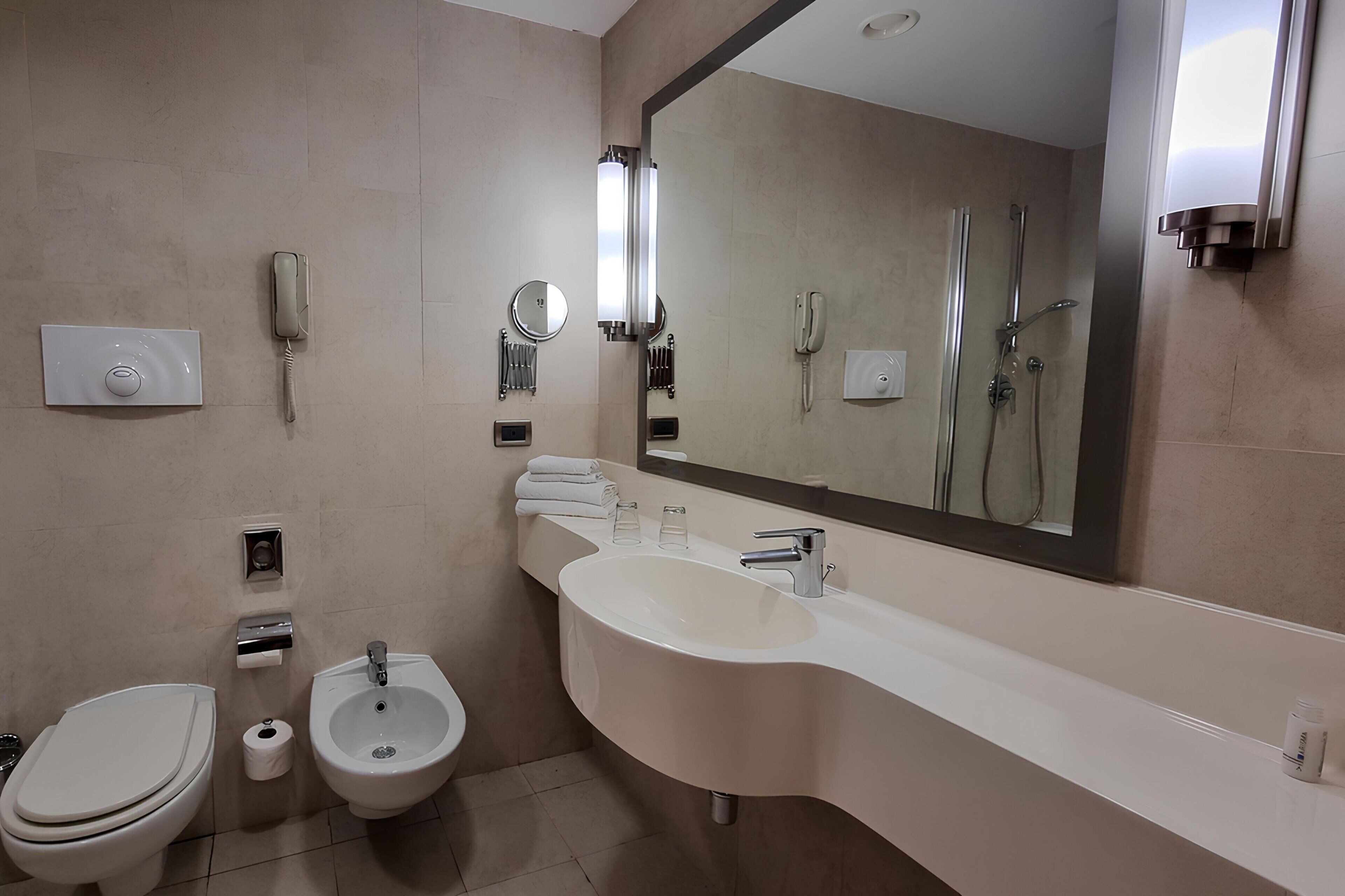 A modern bathroom with a toilet, bidet, sink, and a large mirror.