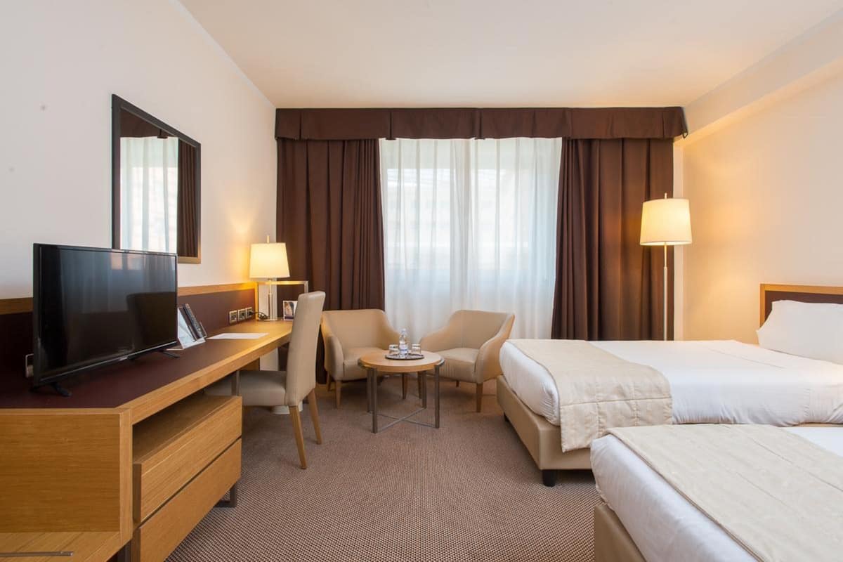 Habitación de hotel con televisión, escritorio, dos sillas, una mesita y dos camas.