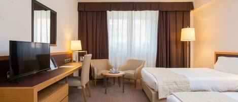 A hotel room with a TV, a desk, two chairs, a small table, and two beds.
