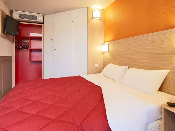 A hotel room with a bed, a TV mounted on the wall, and a wardrobe.