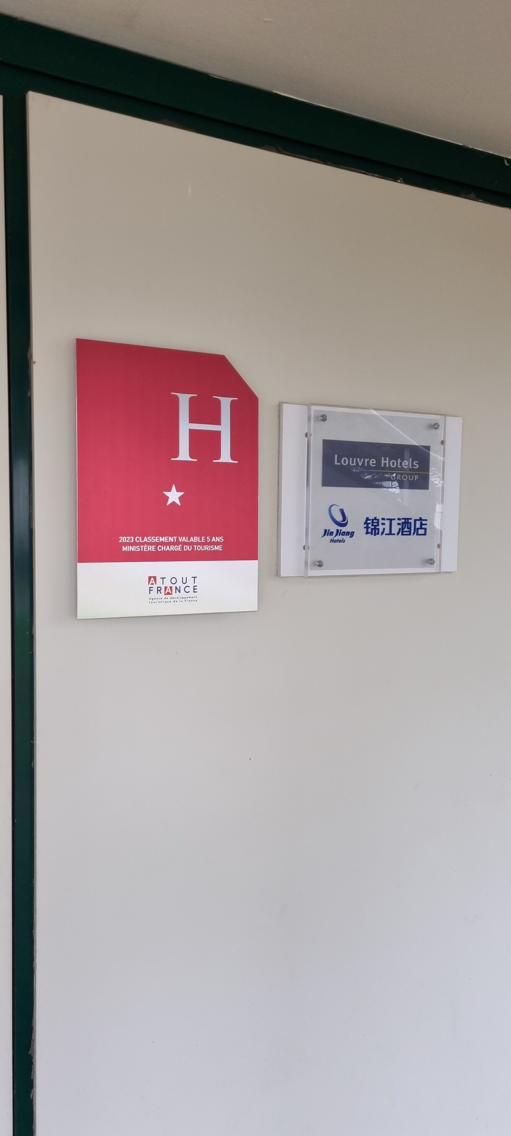 Two signs on a wall: one is a red sign with a white 'H' and a star, and the other is a white sign with 'Louvre Hotels' and 'Jin Long Hotels' logos.