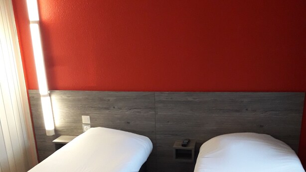 Two single beds with white linens in a room with red walls and wooden flooring. - Premiere Classe Rouen Sud - Oissel (Saint-Etienne-du-Rouvray)
