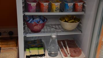 Uma geladeira com diversos alimentos, incluindo iogurte, queijo, presunto e acompanhamentos.