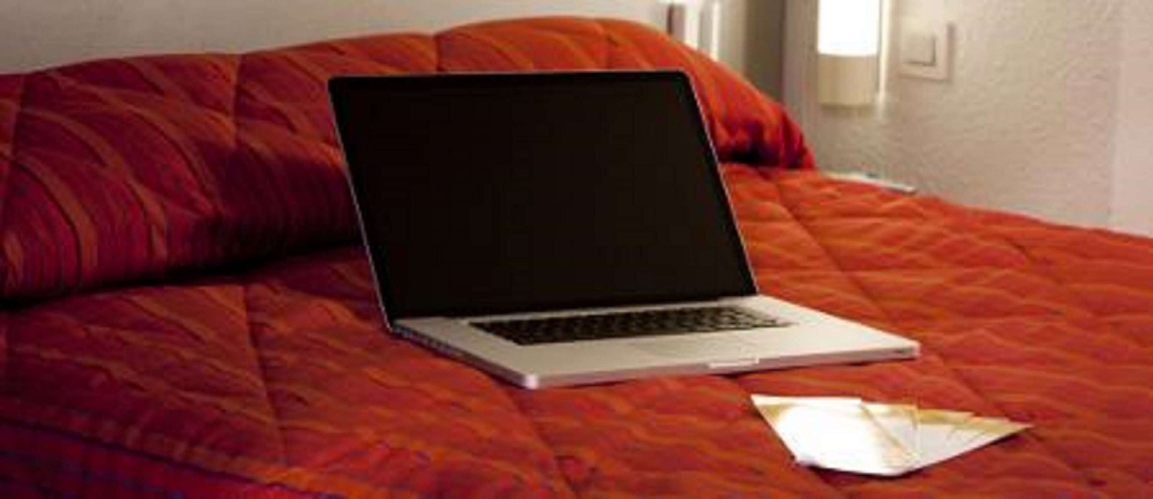 A laptop on a bed with a red blanket.