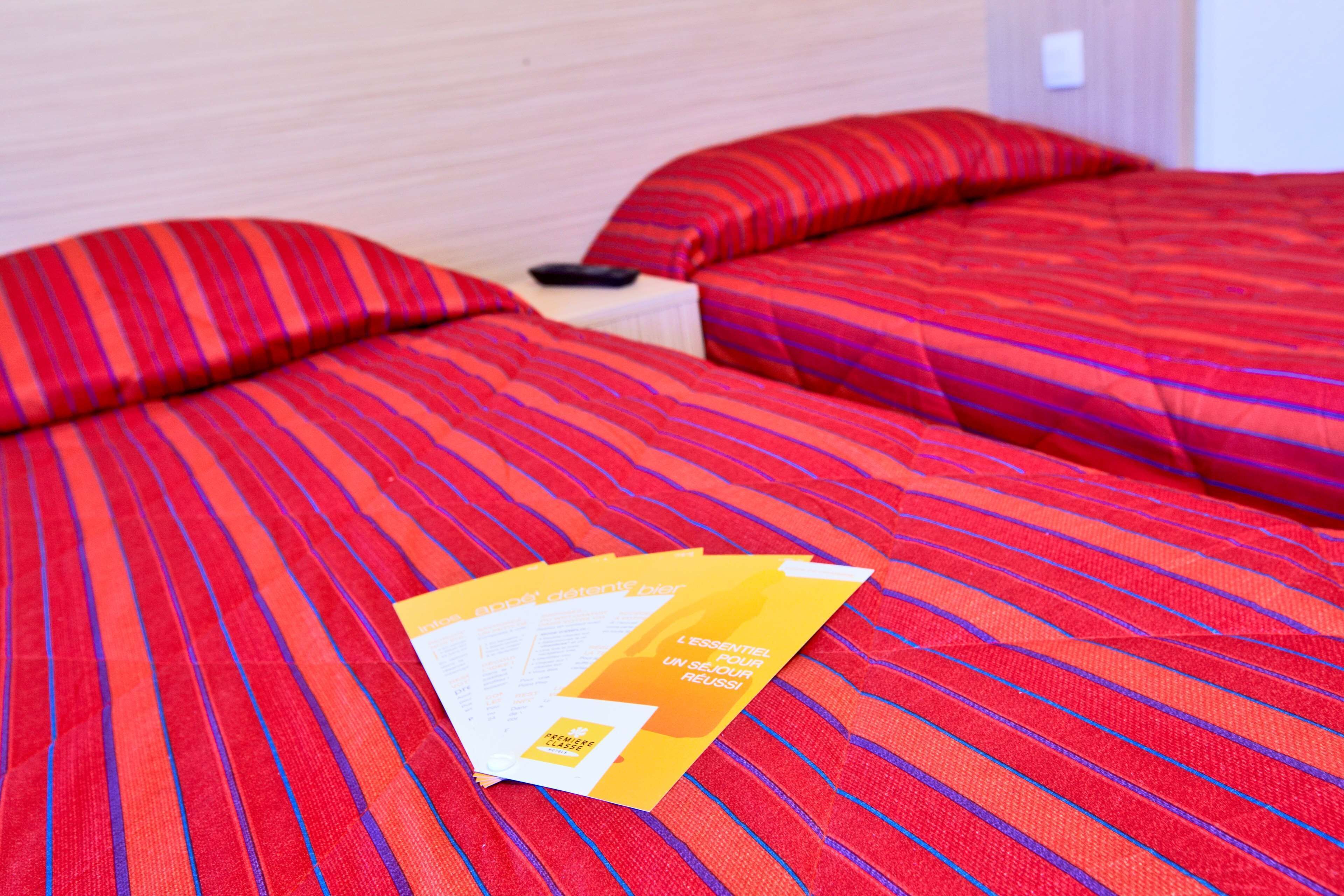 A hotel room with two beds, each with red striped bedding. There are brochures on the beds.
