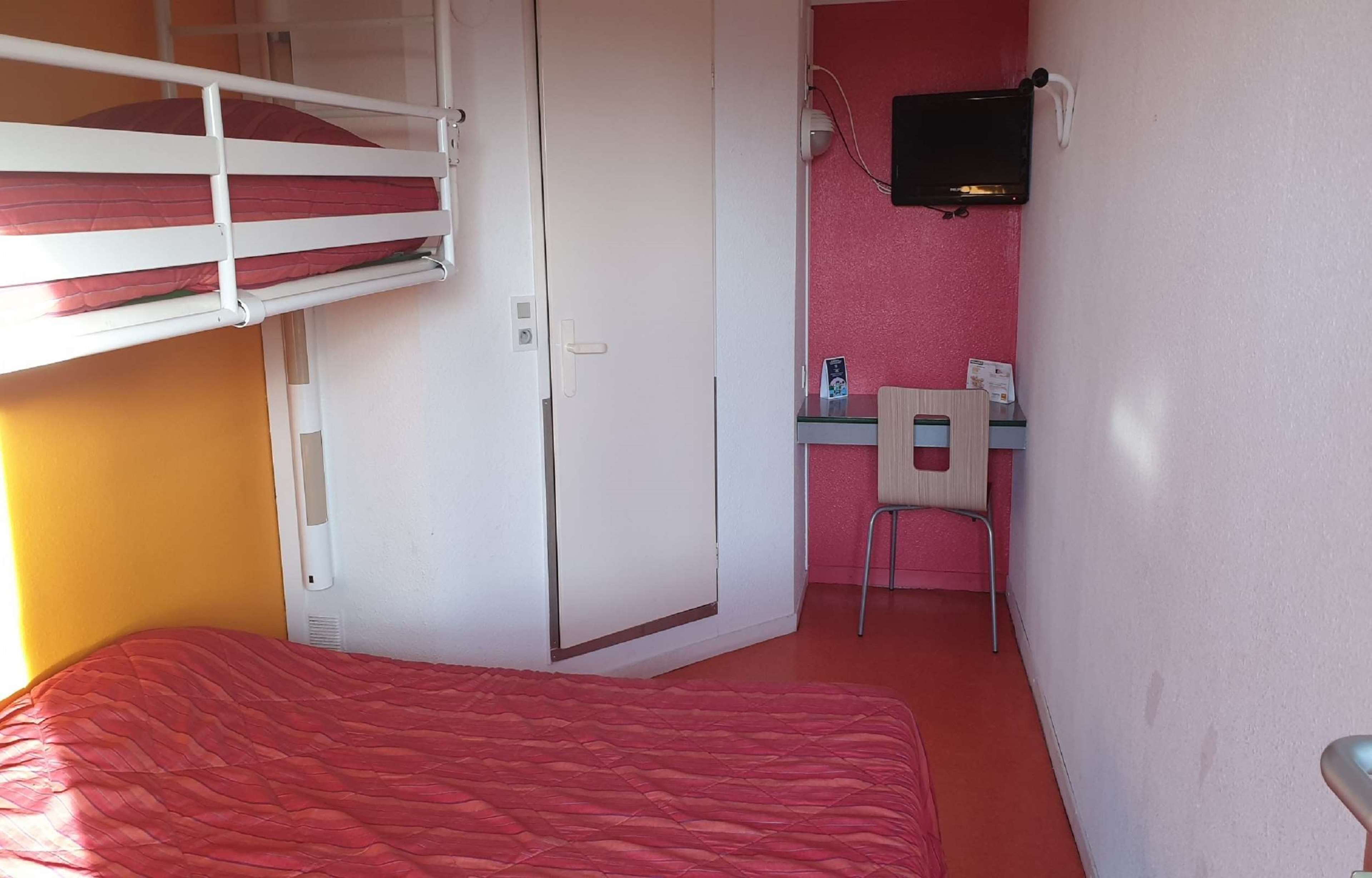 A room with a bunk bed, a desk with a chair, and a television mounted on the wall.