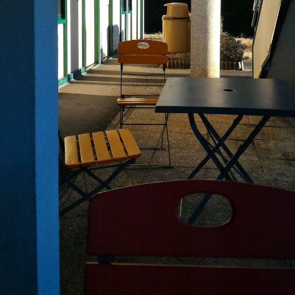 An outdoor seating area with a table and chairs, a trash can, and a building in the background. - Premiere Classe Vierzon (Vierzon)