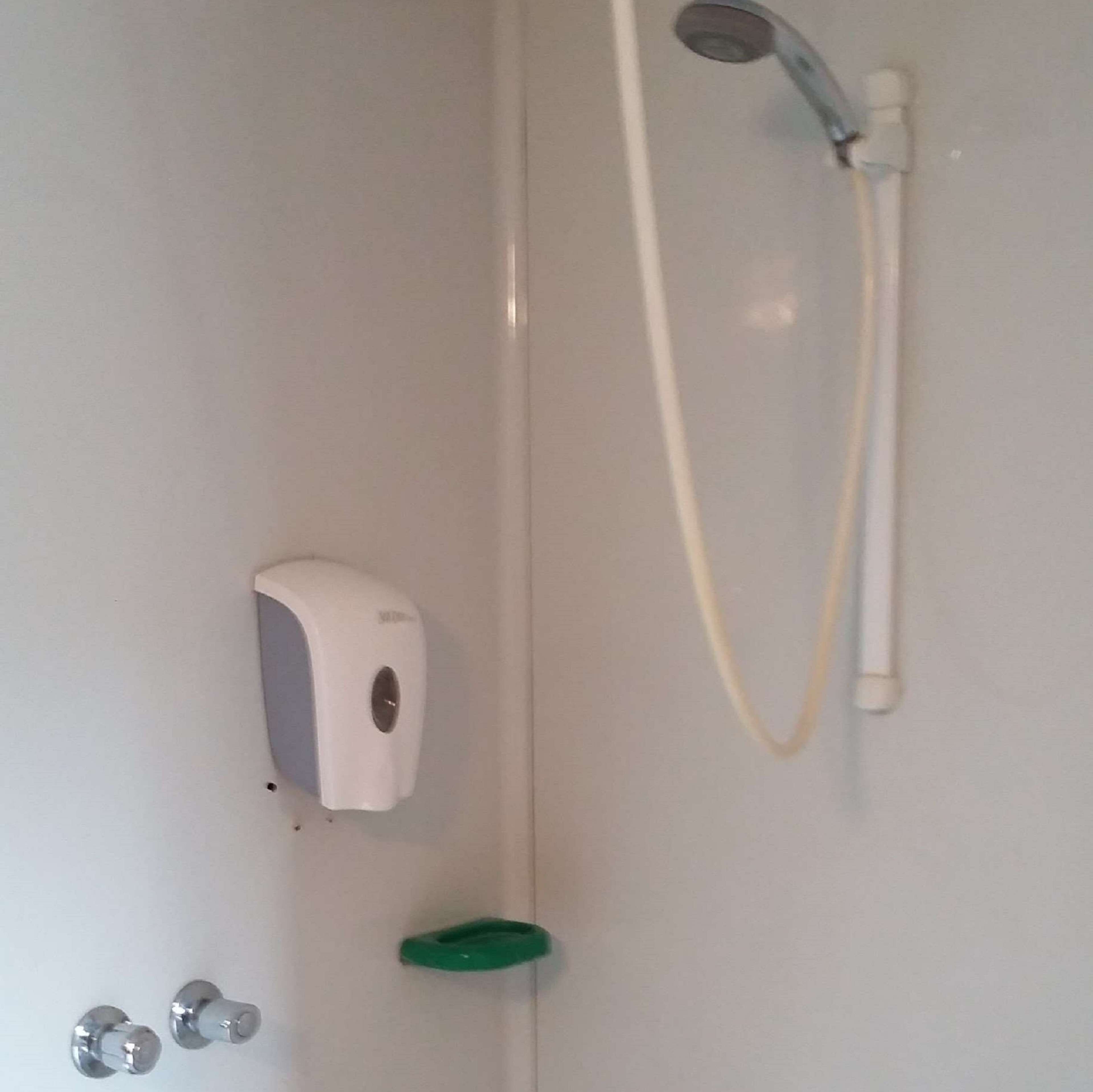 Baño con dispensador de jabón para manos, cabezal de ducha y un asa verde.