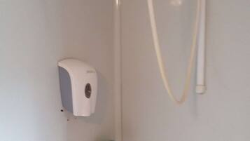 A bathroom with a hand soap dispenser, a shower head, and a green handle.