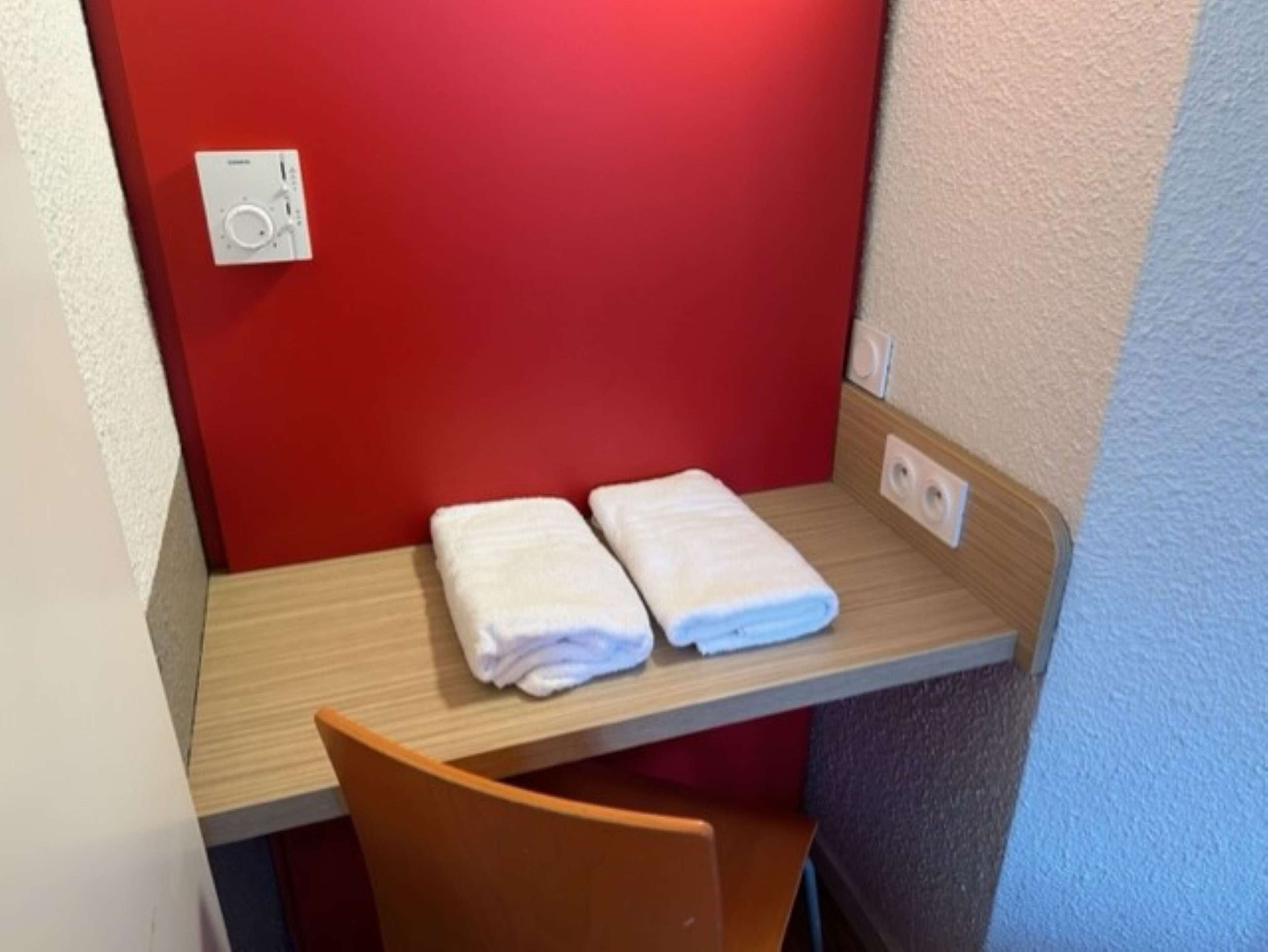 Una habitación pequeña con una pared roja, un escritorio de madera y dos toallas blancas dobladas con cuidado sobre el escritorio.