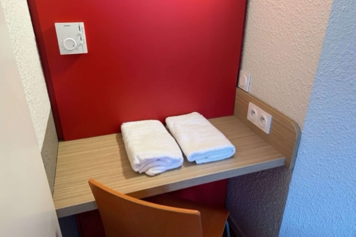 Ein kleiner Raum mit roter Wand, einem Holztisch und zwei ordentlich gefalteten weißen Handtüchern auf dem Tisch.