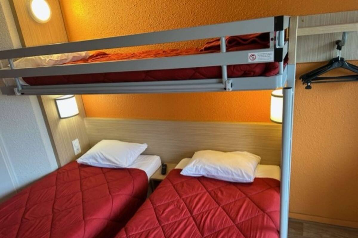 A bunk bed with red bedding, a wooden headboard, and a wall-mounted light.