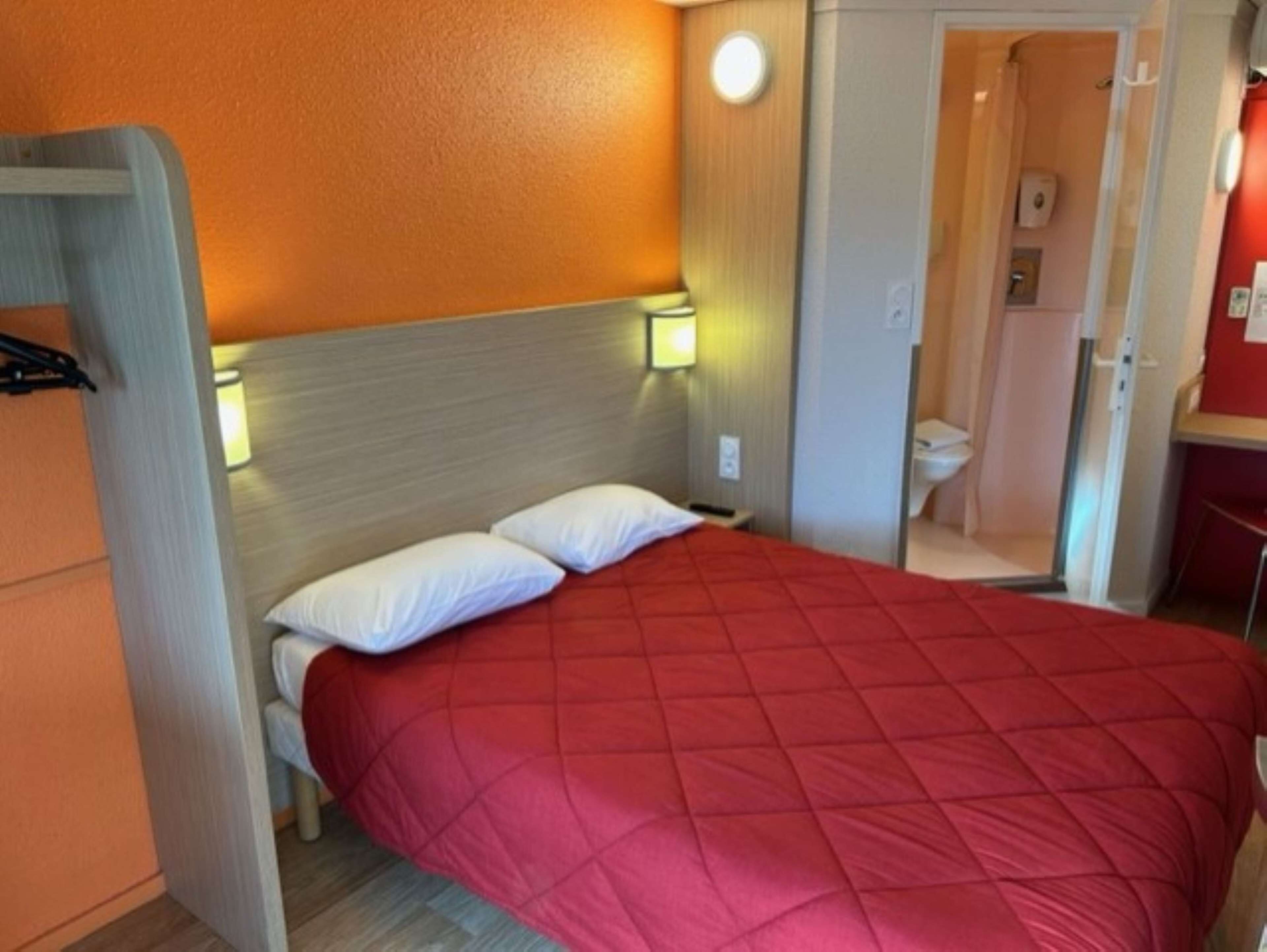 Una habitación de hotel con una cama, dos lámparas de noche y un cabecero de madera.