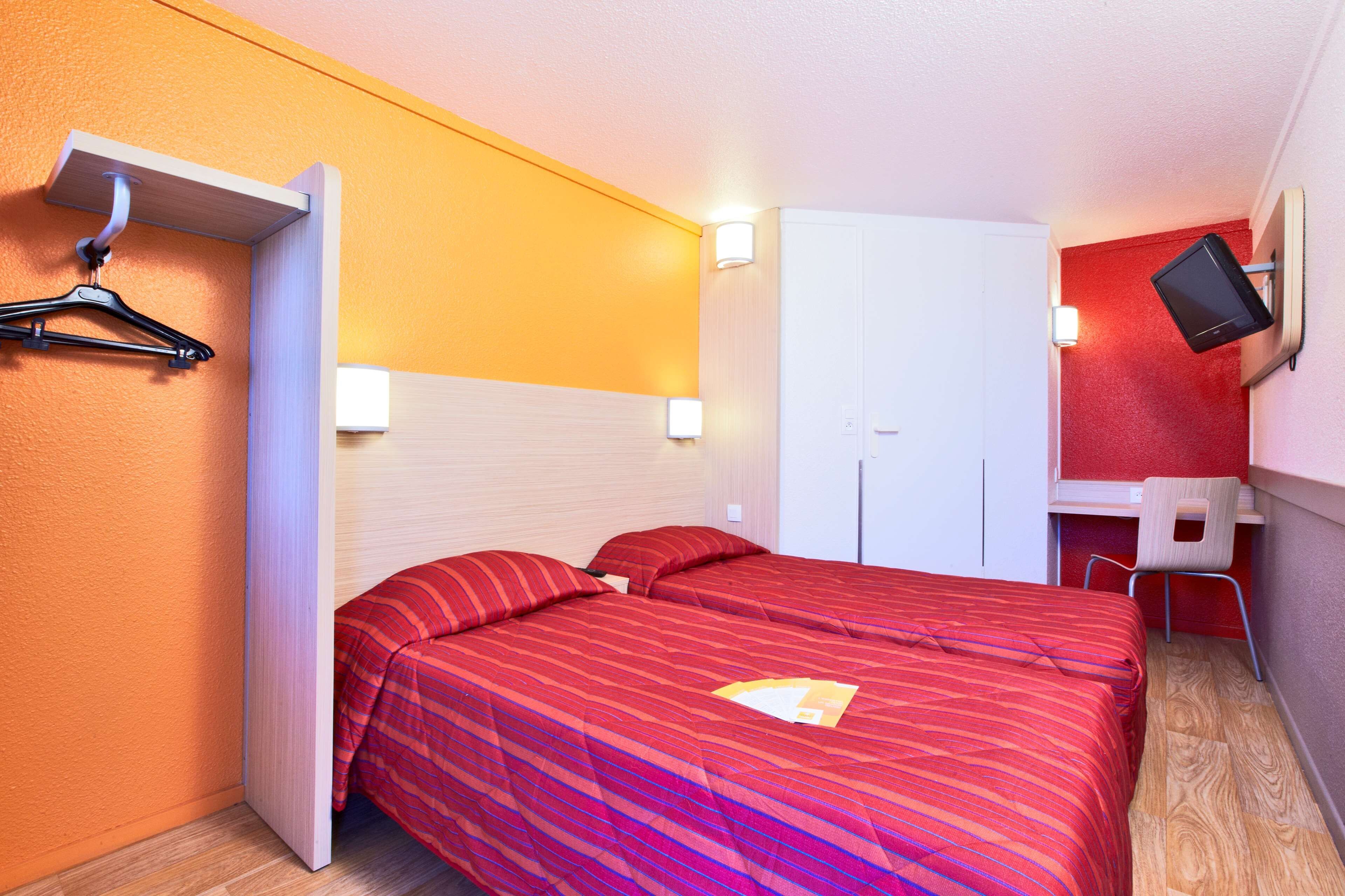 Une chambre d’hôtel comprenant un lit, un bureau, une chaise, une télévision et une armoire.