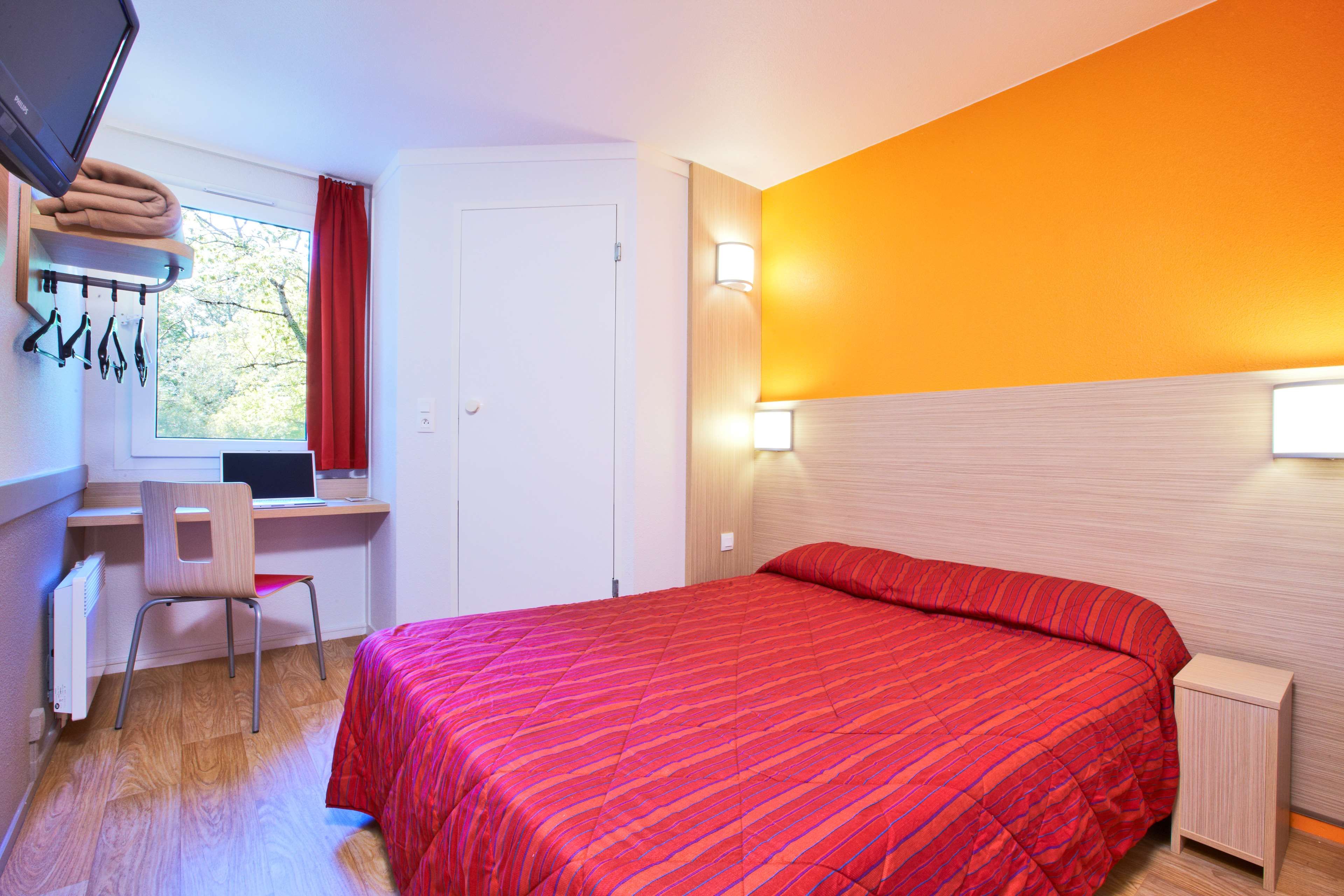 Ein Hotelzimmer mit einem Bett, einem Schreibtisch, einem Stuhl, einem Vorhangfenster und einer Wandlampe.
