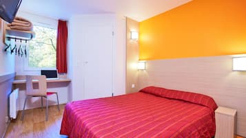 Ein Hotelzimmer mit einem Bett, einem Schreibtisch, einem Stuhl, einem Vorhangfenster und einer Wandlampe.