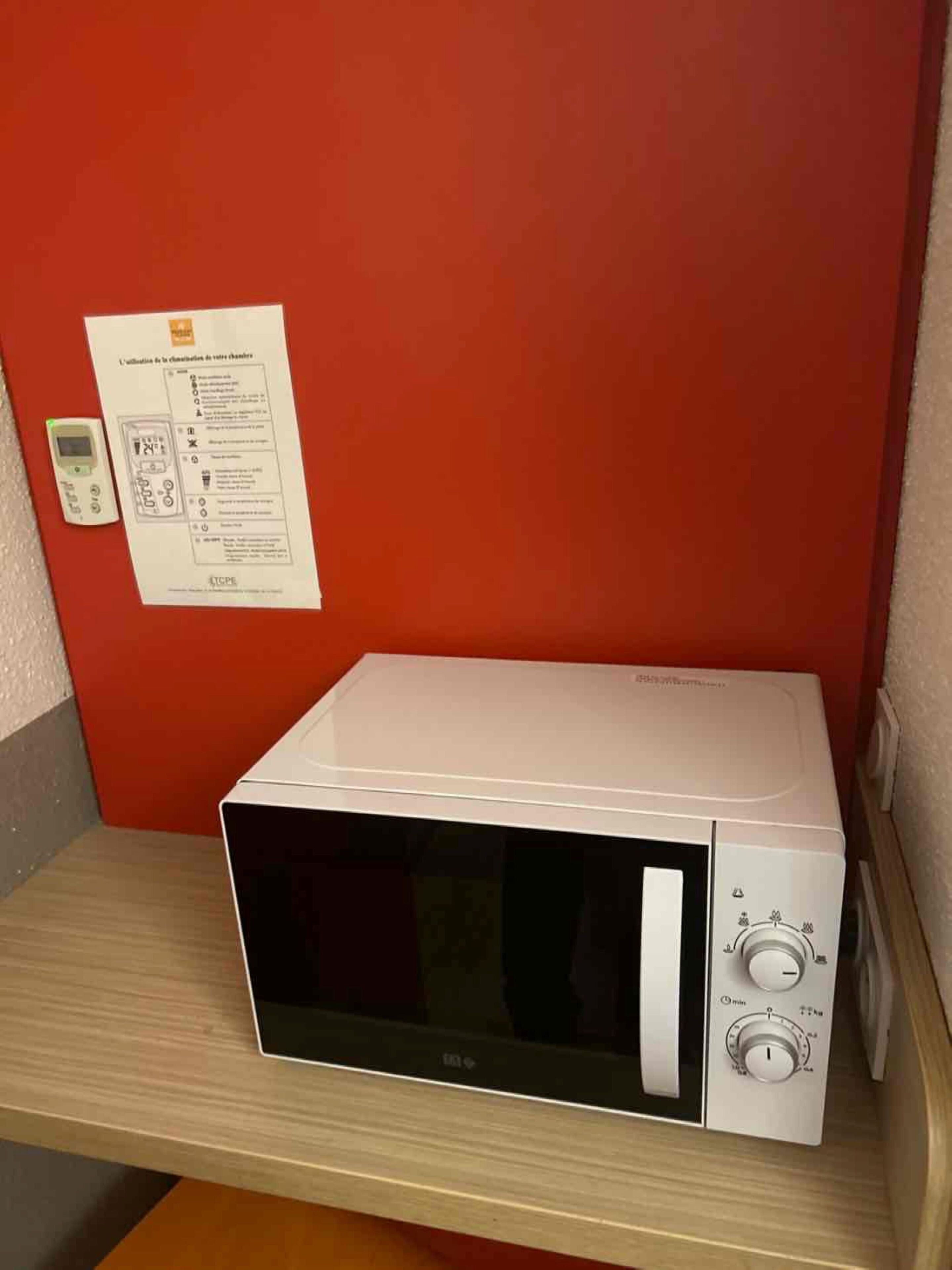 Un microondas sobre una repisa de madera en una habitación con pared roja.