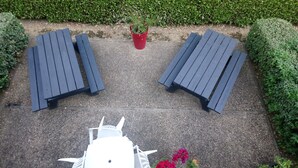 Un espacio al aire libre con dos mesas y sillas de madera oscura, rodeado de follaje.