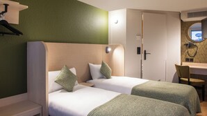 Ein Hotelzimmer mit zwei Betten, einem Schreibtisch, einem Stuhl und einem Badezimmer mit Spiegel.
