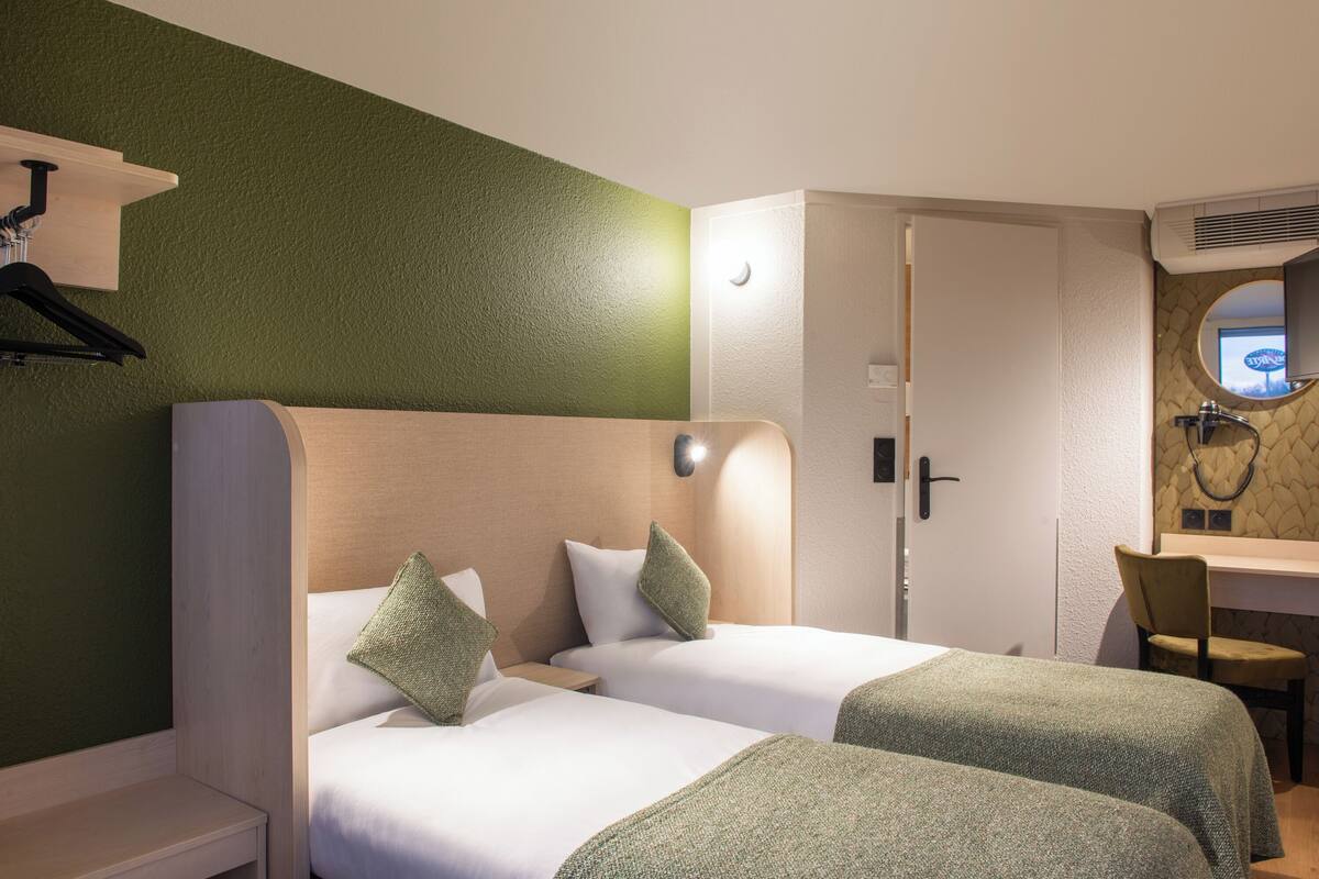 Une chambre d’hôtel avec deux lits, un bureau, une chaise et une salle de bain avec un miroir.