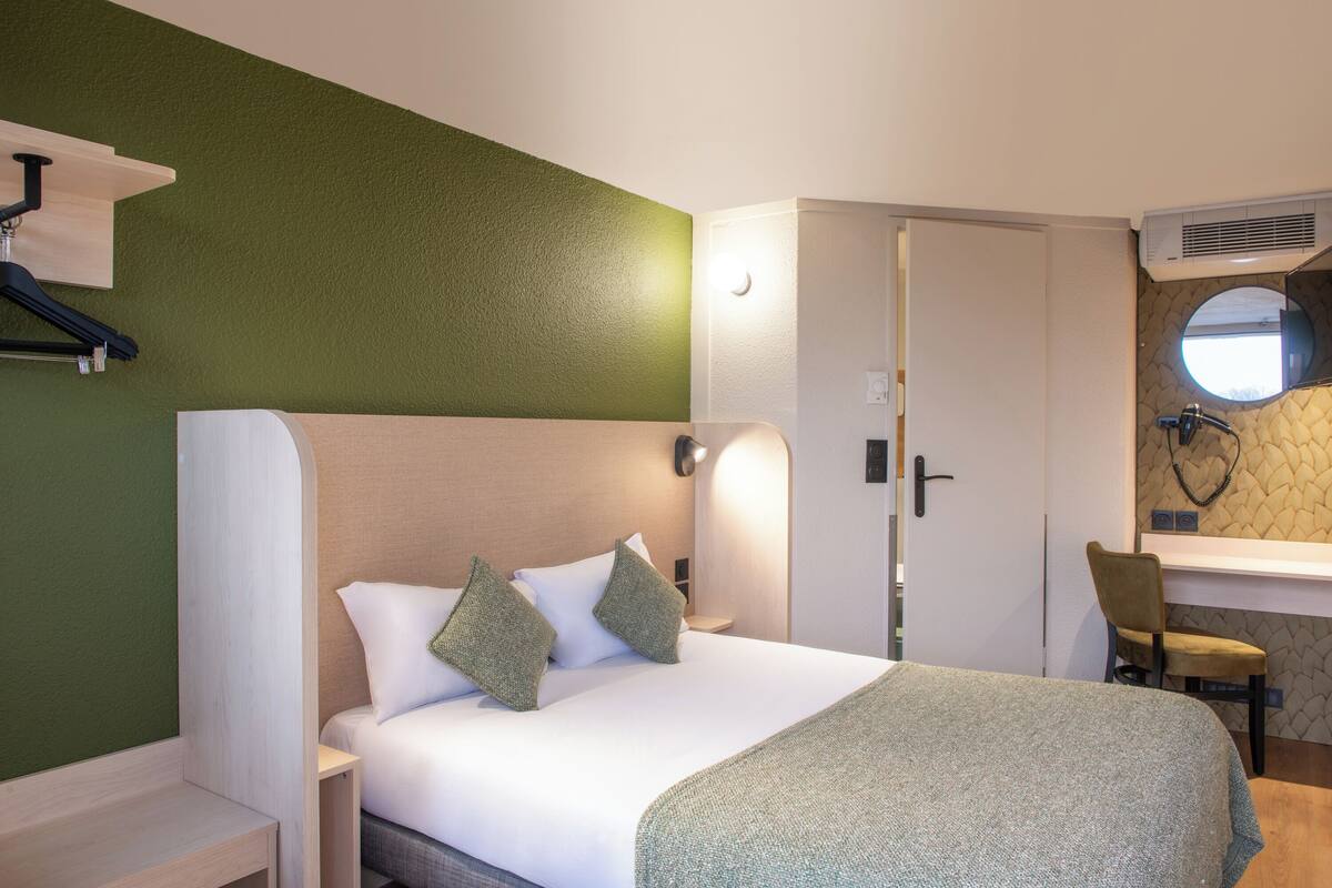 Une chambre d’hôtel comprenant un lit, une table de chevet, une chaise, un bureau et un miroir.