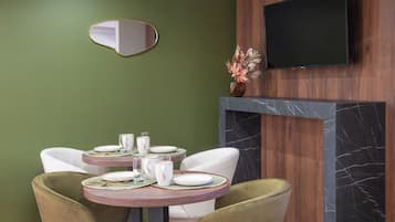 Un coin repas avec une table ronde dressée pour quatre personnes, entourée de chaises blanches, un mur décoratif en bois et un téléviseur à écran plat fixé au-dessus d’une cheminée.