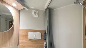 Ein kleines Badezimmer mit Toilette, Holzwaschtisch, Spiegel, Duschkabine und einer Steckdose.