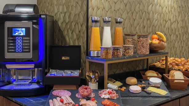 Ein Frühstücksbuffet mit verschiedenen Speisen, einer Kaffeemaschine und einer Obstschale.
