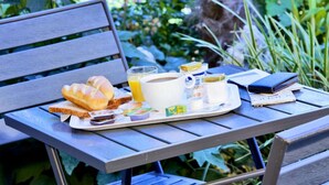 A breakfast tray on a wooden table outdoors with bread, a glass of orange juice, a mug, and some packaged food items. - Premiere Classe Bourges (6 kms du centre-ville) (Bourges)