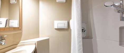 Un baño moderno con lavamanos, espejo, dispensador de toallas y ducha.