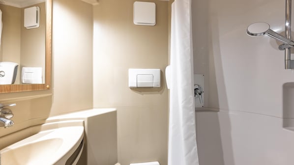 Un baño moderno con lavamanos, espejo, dispensador de toallas y ducha.