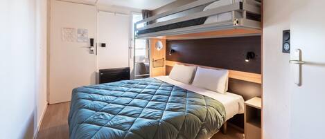 Habitación de hotel compacta con literas, una cama individual, una mesita de noche y un escritorio pequeño.