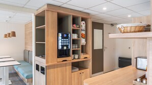 A modern kitchenette with a built-in coffee machine, a small refrigerator, and a shelf with kitchen essentials. - Premiere Classe Bourges (6 kms du centre-ville) (Bourges)