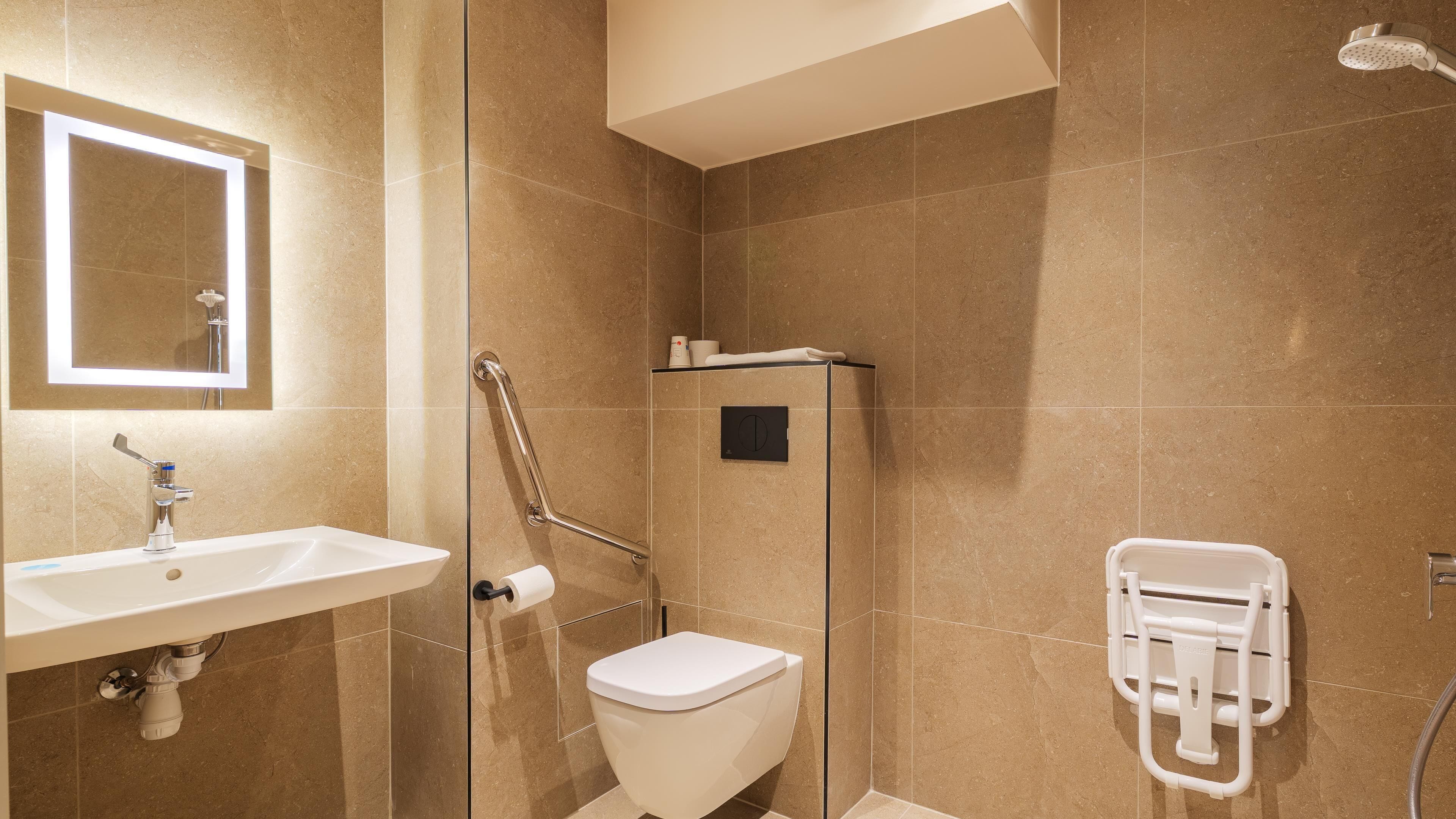 Une salle de bain équipée d’un lavabo, de toilettes, d’une douche et d’une barre d’appui.