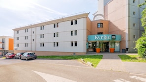 Een meerhoog gebouw met een opvallend 'Kyriad ECO' bord, een parkeerplaats met verschillende auto's en een klein groen gebied met potplanten.
