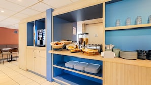 Un espace buffet pour le petit-déjeuner avec une machine à café, des paniers de pain et un distributeur de jus.