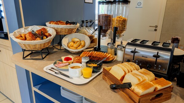 Un bufé de desayuno con pan, bollería y una máquina de café.
