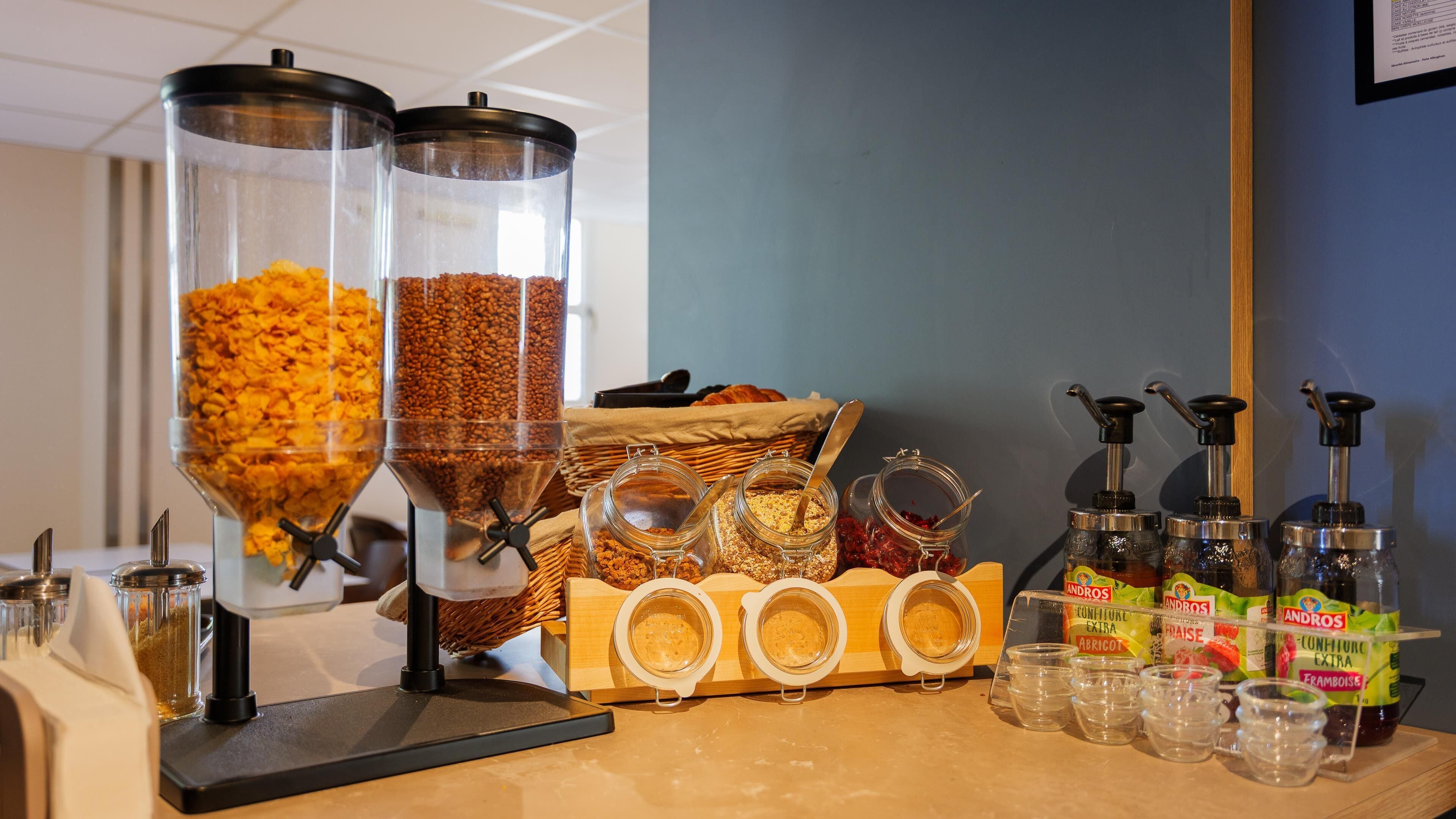 A breakfast bar with various food dispensers, jars of condiments, and a basket of bread.