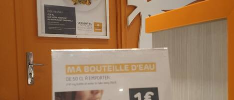 Uma área de recepção de hotel, com uma garrafa de água e um cartaz anunciando 15% de desconto no restaurante.