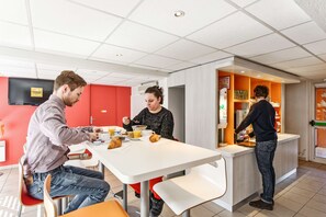 Een moderne eethoek met een witte tafel, rode wanden en een persoon die eten bereidt aan een aanrecht.