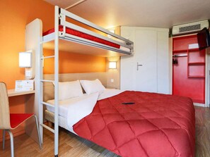 Uma cama beliche com colchão vermelho, uma escrivaninha com cadeira e um guarda-roupa com porta vermelha.