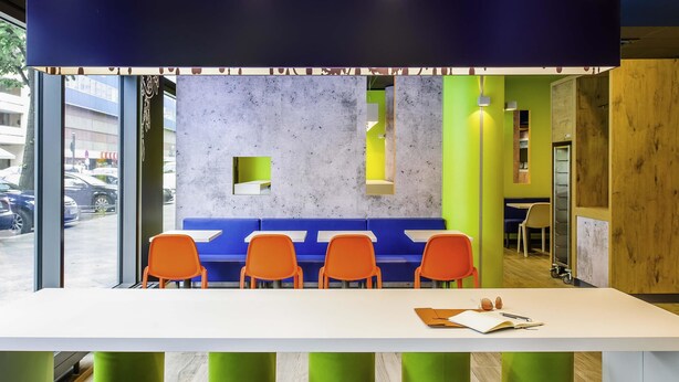 A modern seating area with a white table, blue and orange chairs, and green stools.