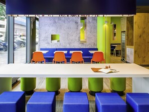 A modern seating area with a white table, blue and orange chairs, and green stools. - ibis Budget Marne-la-Vallée Noisy-le-Grand (Noisy-le-Grand)