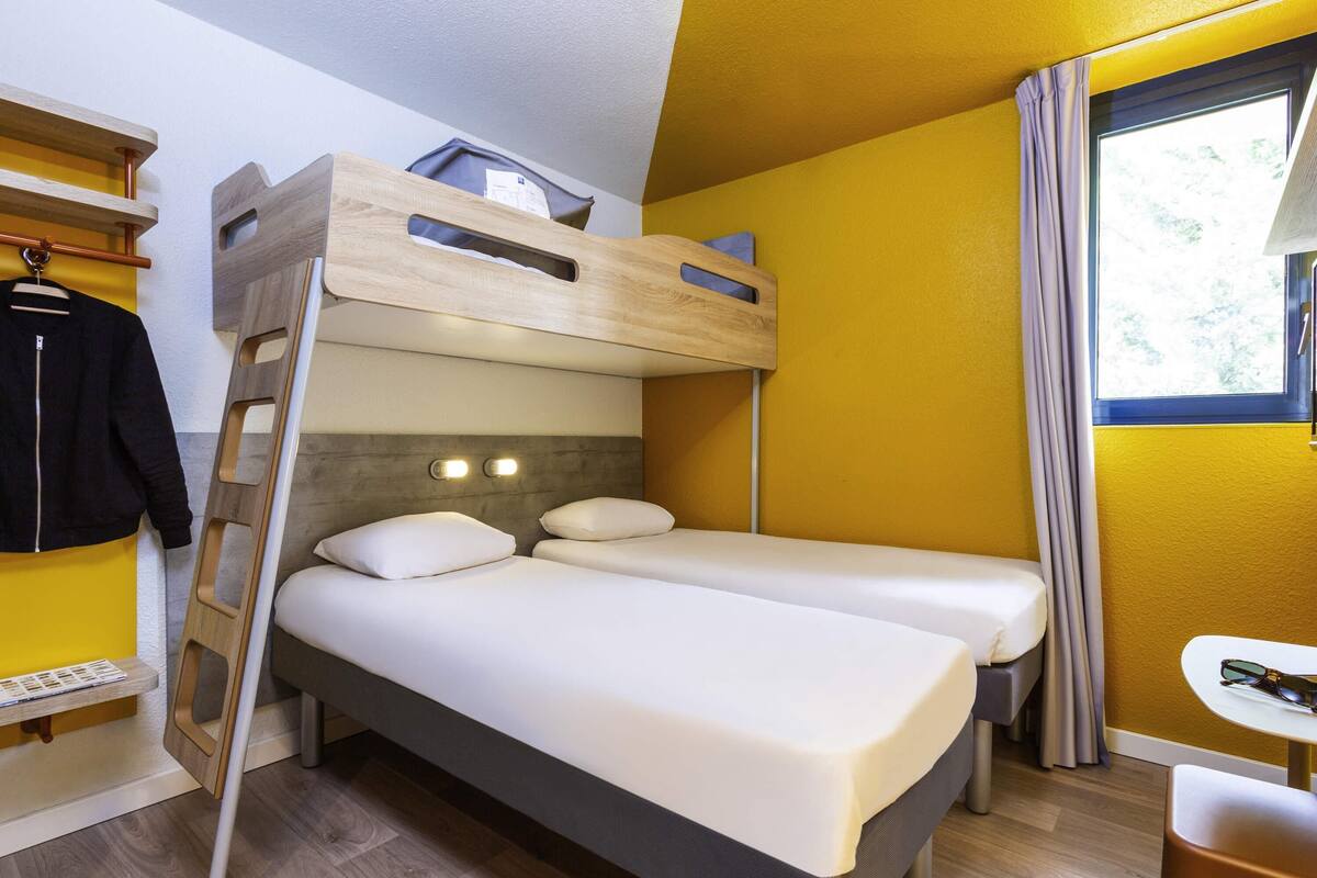 A bunk bed room with a ladder, a small table, and a window with curtains.