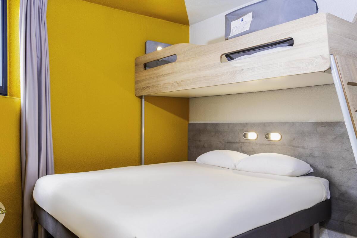 A bed with a headboard, a wooden shelf above, and a curtain on the left.