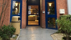 A hotel entrance with a blue and red facade, a sign for 'ibis budget hotels', and a visible reception area.