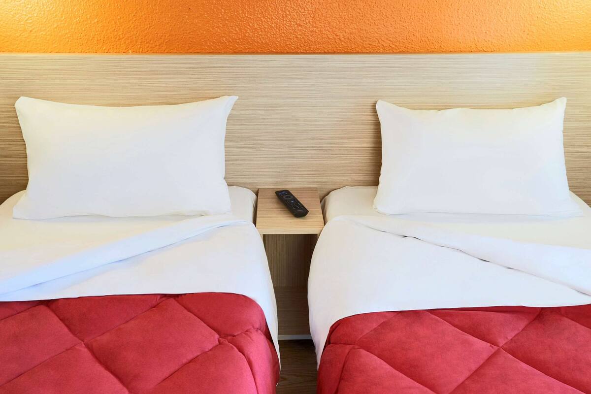 Two single beds with white linens and red headboards, a wooden headboard, and a remote control on a wooden nightstand.