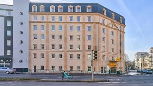 Un hotel de varios pisos con un diseño arquitectónico clásico, que cuenta con una entrada central con dosel amarillo, múltiples ventanas y un techo plano.